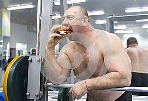 Man eats a hamburger with meat and cheese in the gym