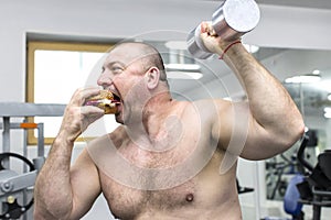 Man eats a hamburger with meat and cheese in the gym