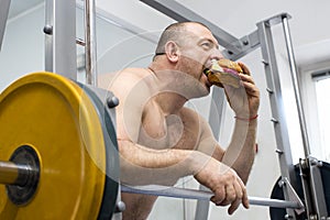 Man eats a hamburger with meat and cheese in the gym