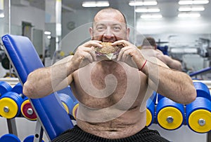 Man eats a hamburger with meat and cheese in the gym