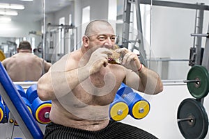 Man eats a hamburger with meat and cheese in the gym