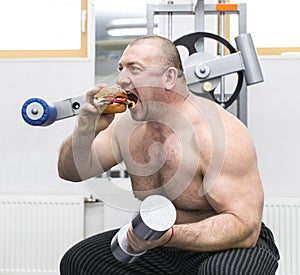 Man eats a hamburger with meat and cheese in the gym