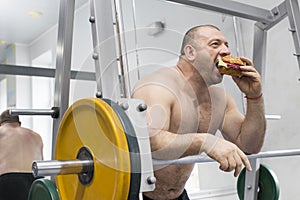 Man eats a hamburger with meat and cheese in the gym