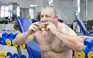 Man eats a hamburger with meat and cheese in the gym