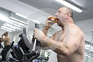 Man eats a hamburger with meat and cheese in the gym