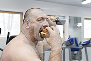 Man eats a hamburger with meat and cheese in the gym