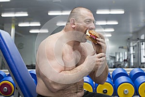 Man eats a hamburger with meat and cheese in the gym