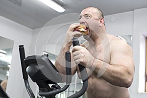 Man eats a hamburger with meat and cheese in the gym