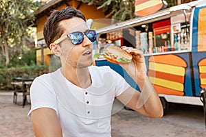 Man eats a hamburger near an outdoor foodtruck. Streetfood and junk food concept