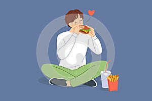 Man eats hamburger with sausage and cheese, sitting on floor and enjoying taste of fast food