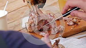 A man eats a huge piece of fried meat on the bone outdoors with a special fork and knife for cutting meat