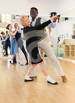 Man and elderly woman performing ballroom dance in dancing room