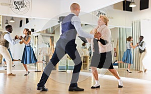 Man and elderly woman performing jazz dance in dancing room