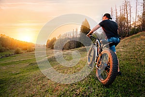 Man with an electric fatbike on the background of the sunset. Picturesque place in the village. Concept of a healthy lifestyle