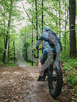 A man on an electric fatbike rides through a wet forest.