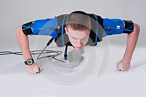 Man in an electric muscular suit for stimulation does push-ups on the fists