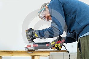 Man with electric saw to cut wooden piece at home. He is wearing protective glasses and gloves