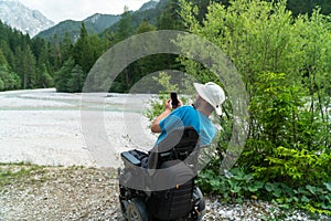 Man on electric wheelchair using smartphone camera in nature