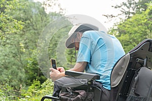 Man on electric wheelchair using smartphone camera in nature