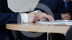 Man in an elegant suit signs or endorses a document during a working meeting or negotiations. No face. Clerk, official, deputy, photo