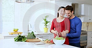 Man embracing pregnant woman while preparing salad at kitchen counter 4k