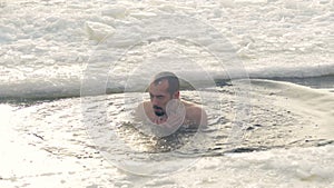 A man emerges from the cold water in an ice hole.