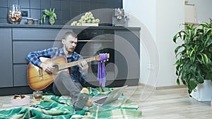 Man emotionally playing on acoustic guitar. Young musician play guitar while sitting on the floor at home. Online guitar lessons.