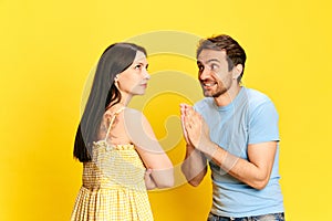 Man emotionally talking to offended woman and asking for forgiveness against yellow studio background