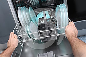 Man empty out the dishwasher in kitchen.Close-up of male hands loading dishes to the dishwasher