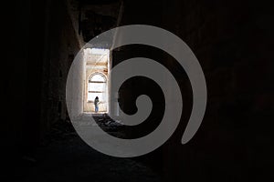 A man at the end of a dark corridor inside an abandoned building.