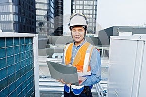 Man engineer holding laptop working at rooftop building construction. Male technician worker working checking hvac of office