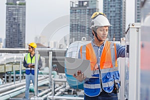 Man engineer holding laptop working at rooftop building construction. Male technician worker working checking hvac of office