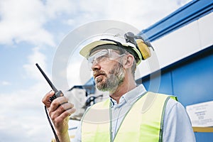 Man engineer wearing a helmet and protective glasses talk on walkie-talkie