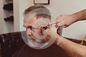 man enjoing haircut by a master in a barbershop.  An old man gets a stylish haircut