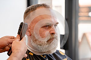 man enjoing haircut by a master in a barbershop. An old man gets a stylish haircut