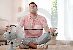 Man enjoying air flow from fan on floor in living room. Summer heat