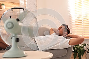 Man enjoying air flow from fan on sofa in living room. Summer heat