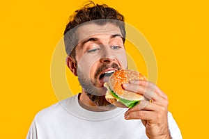 Man enjoying cheeseburger on cheat day on vibrant yellow backdrop