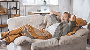 Man enjoying peaceful moment home, laying comfortably on sofa. Concept of freelancing and working from home, which has