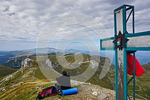 Man enjoying the view on a peak marked by a cross in the mountains