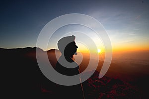 Man enjoying watching beautiful cloudscape sunrise on top of mountain cliff.
