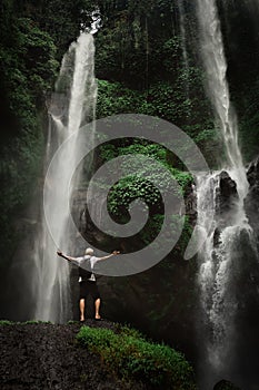 Man enjoying waterfall raised hands. Travel Lifestyle and success concept vacations into the wild nature on background