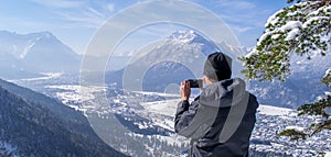 Man enjoys the view and looks down on Garmisch-Partenkirchen and Farchant and takes pictures with his smartphone