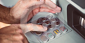 Man entering a PIN code for his credit card at an ATM, withdrawing money, finance concept