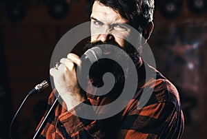 Man with enthusiastic face holds microphone, singing song, karaoke club background. Musician with beard and mustache