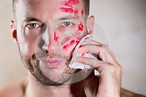 A man erases traces of lipstick from his face with a wet towel