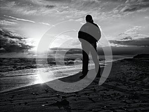 Man at evening sea. Hiker with backpack with hands in pocket along beach.