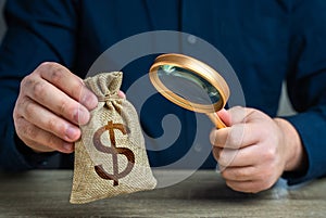 A man examines a dollar money bag through a magnifying glass.