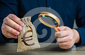 A man examines a euro money bag with a magnifying glass. Checking the origin of capital. Anti money laundering, tax evasion. Study photo