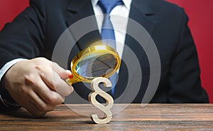 A man examines a paragraph figure with a magnifying glass. Studying laws and legislation, norms, rules. Legal service, lawyer